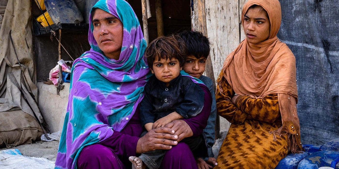 An Afghan woman with three of her children sitting in front of their tented shelter. The mother and the daughter are looking at something to their left, while the two sons are looking into the camera.