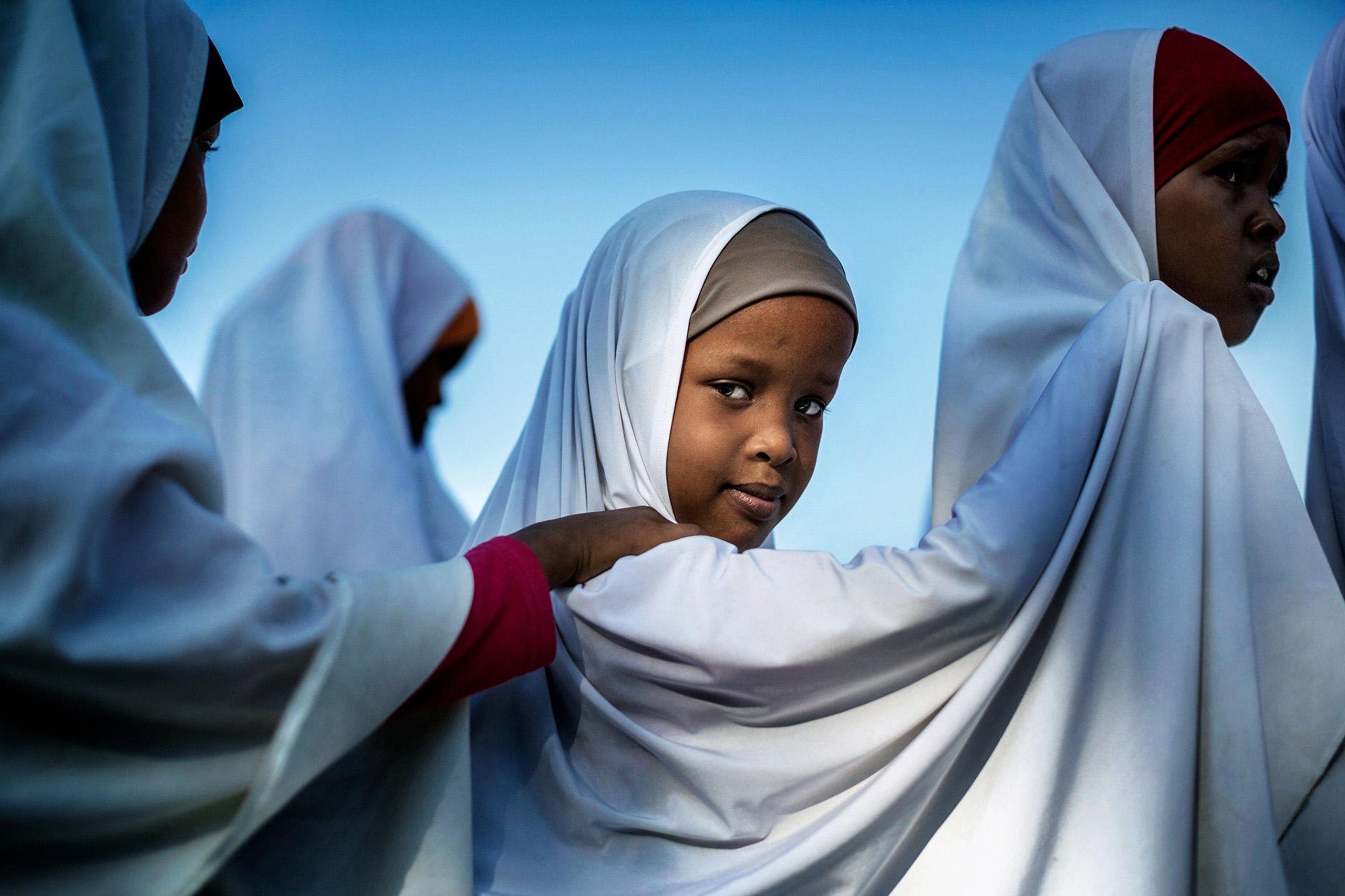 Girls standing in line. One of them is turned towards the camera.