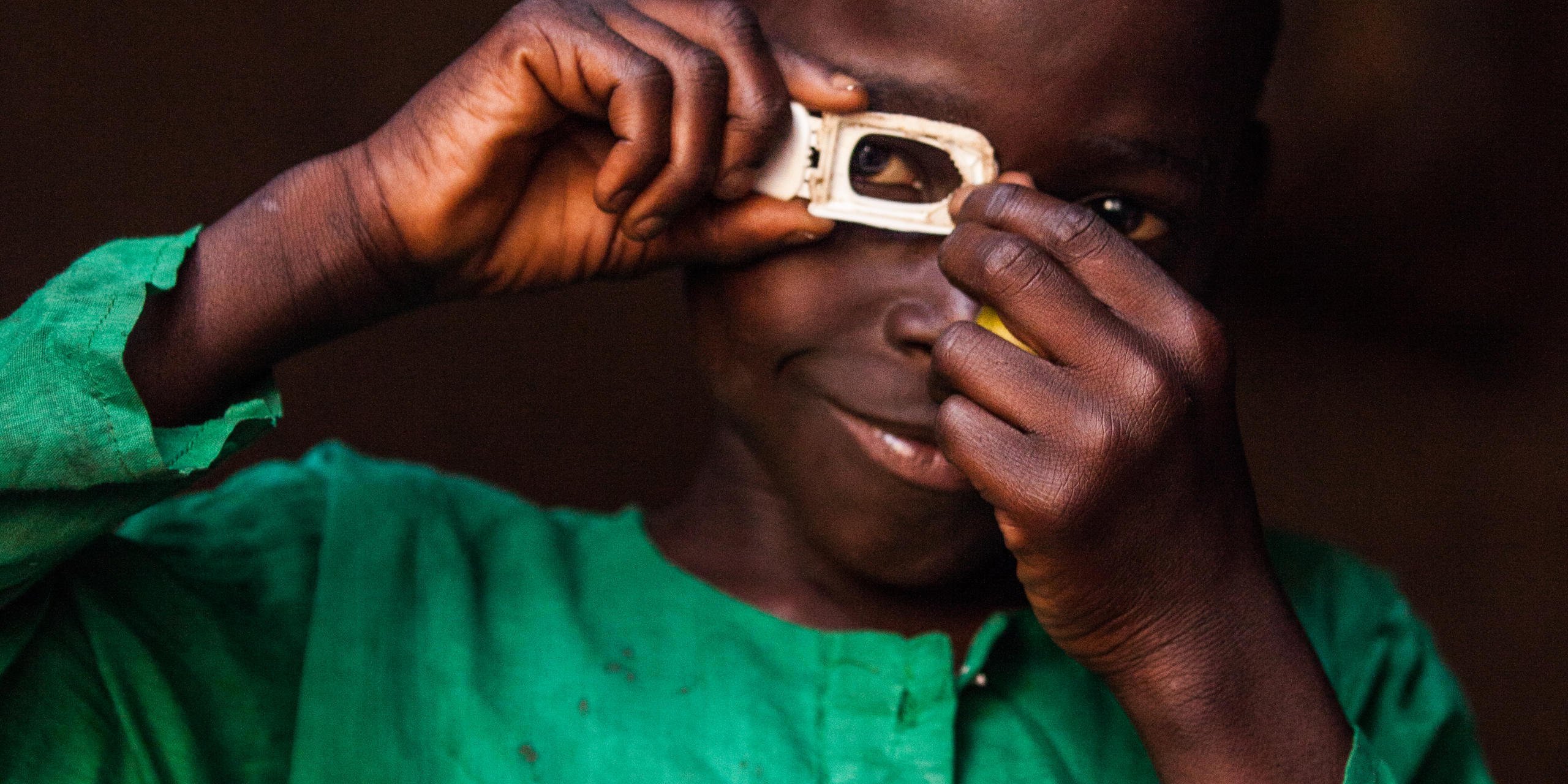 A child in a bright green shirt holding a piece of plastic in front of his eyes and looking through it.