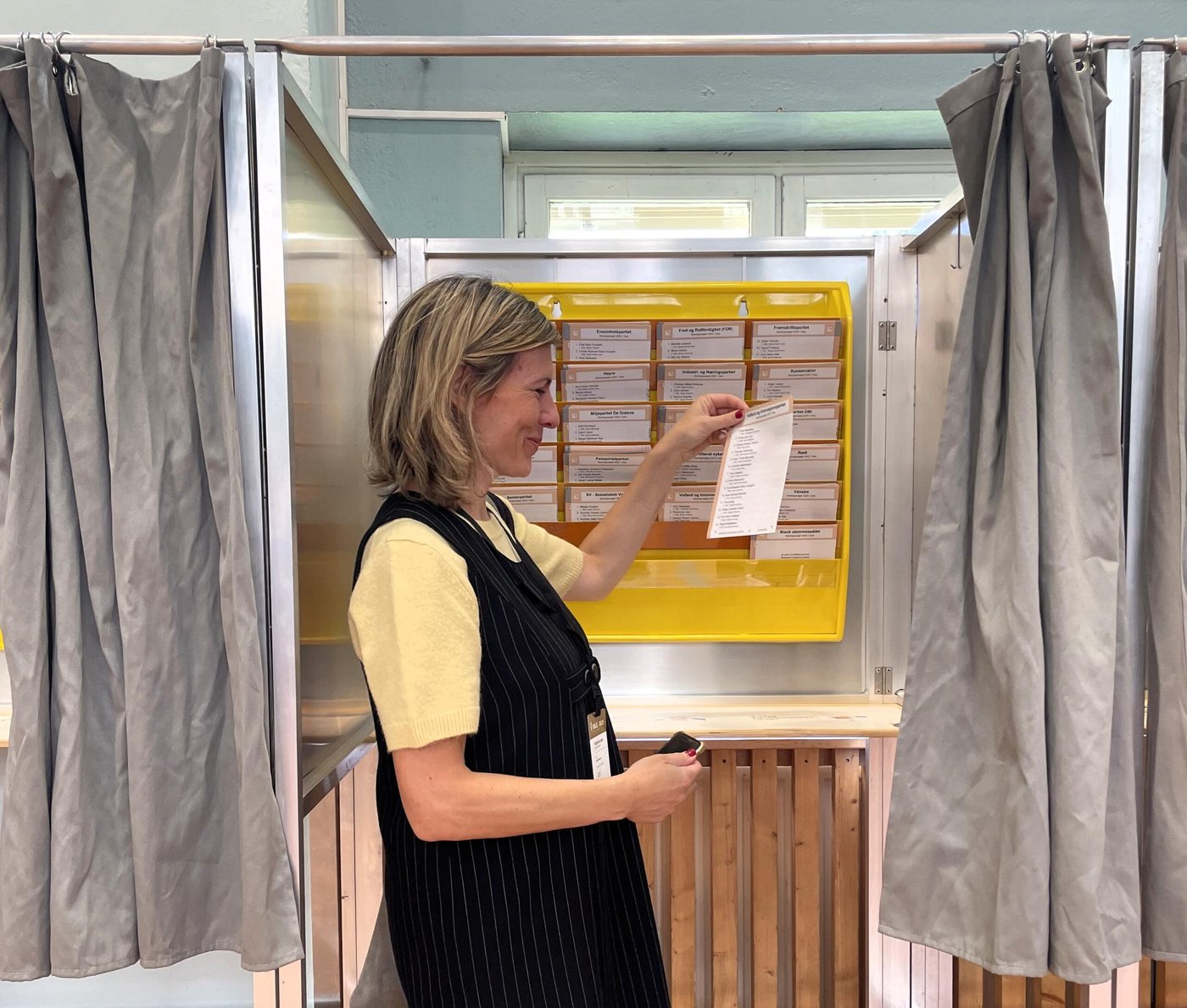 Woman looking at election ballots in an election booth in a voting station in Oslo, Norway. She is holding it up and smiling. 