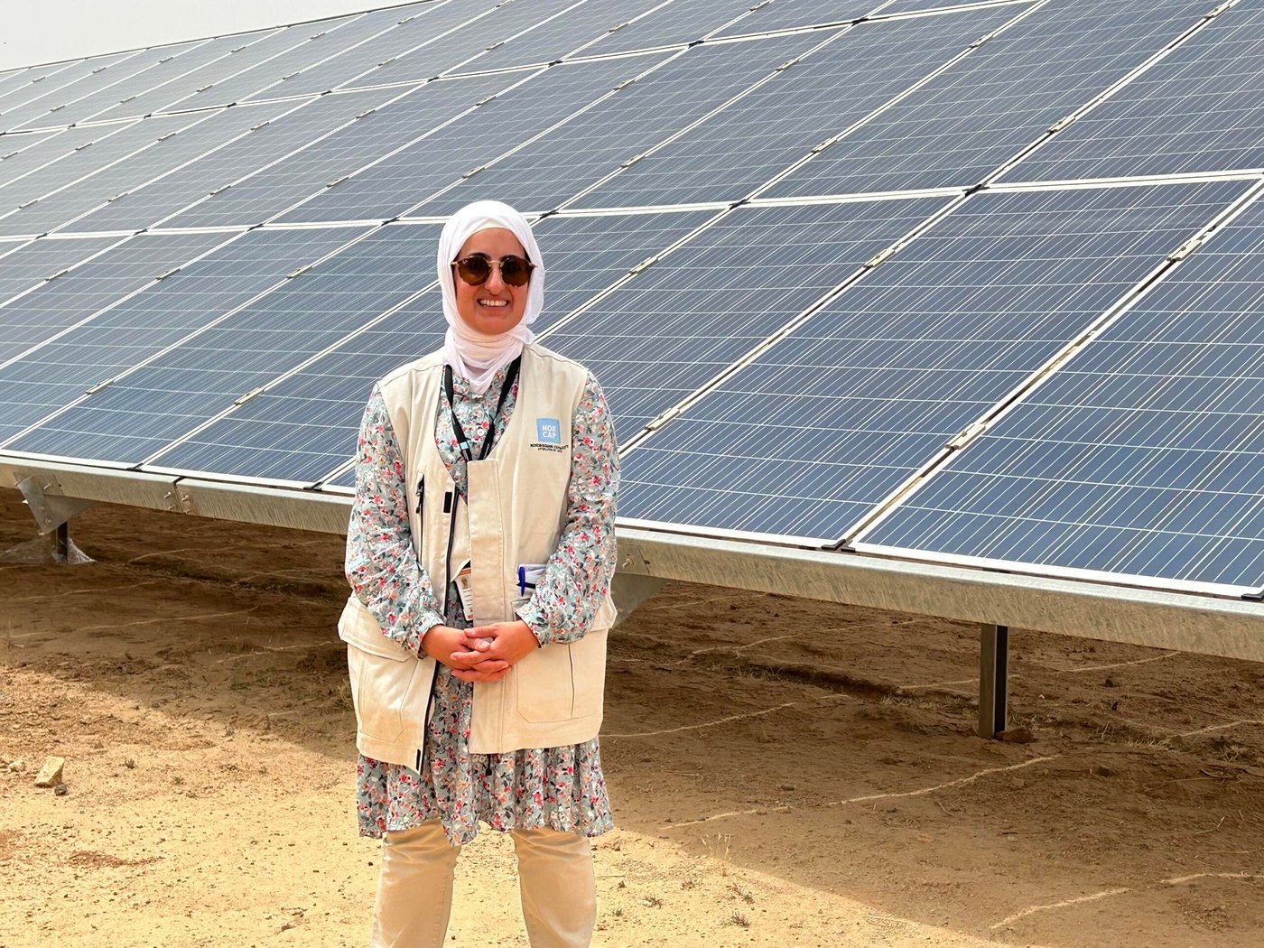 Woman in sunglasses standing in front of a giant solar panel. 