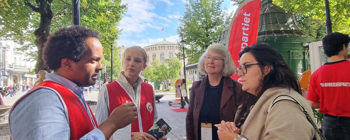 Two campaigners from the Norwegian Labour party, a young man and young woman, talking to two election observers on the streets of Oslo. Parliament in the background.