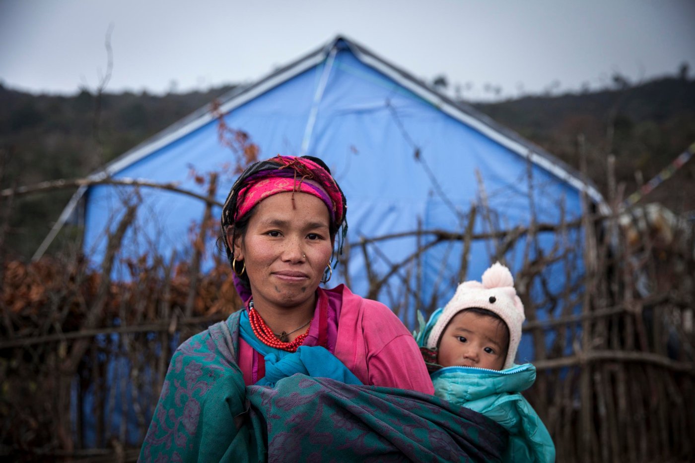 Kanchhi Gole (30) had to run through a combined landslide and earthquake with her then three-month-old daughter Phurba (1) when the earthquake hit Nepal in April last year. (2015) Her husband was in the fields. They lost everything. Since then they have been living in Selang IDP-camp.
"The landslide burried everything. It was so scary. Our home was destroyed. This place is safer. There are aftershocks, but we are not really scared. We are just worried that the snow will bury us, because the roof is not strong enough to hold the weight of the snow", she says.
NORCAP experts working with IOM have distributed tents and tarps, and blankets to help shield against the cold. But the IDPs would like corrugated iron sheets for their roofs, to keep the snow out.
"We don't have enough warm clothes. I only have two sets of clothes for my daughter. We are suffering, but at least we are alive. There is no other option", she says. (Photo: NORCAP/Kishor Sharma)