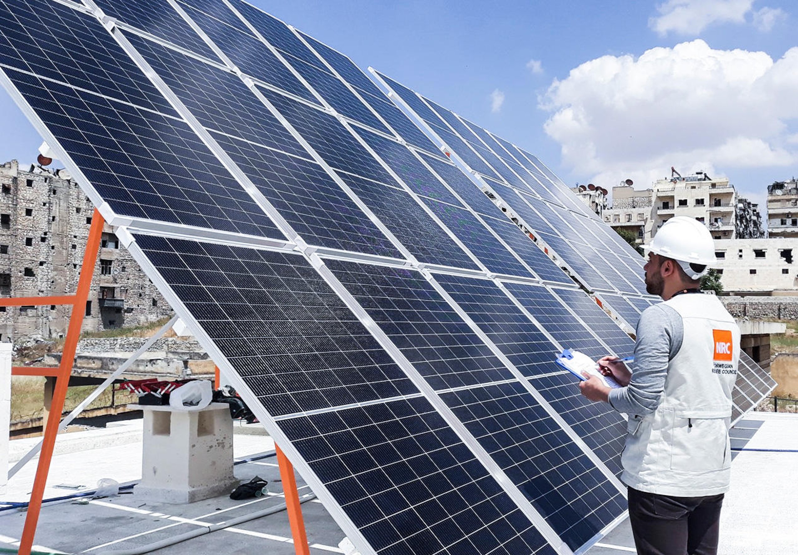 A man with an NRC vest and helmet standing in front of a large solar panel.