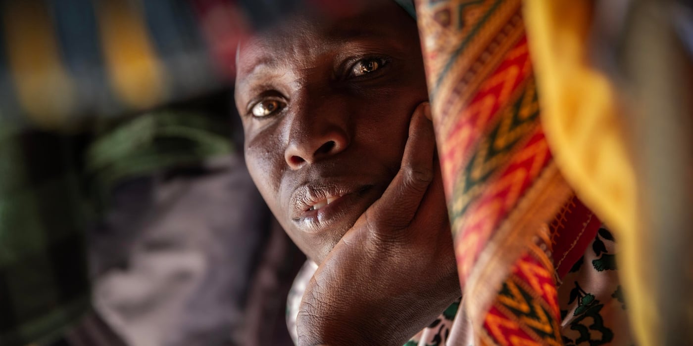 Portrait of a woman resting her head in her hand, surrounded by colourful fabrics.