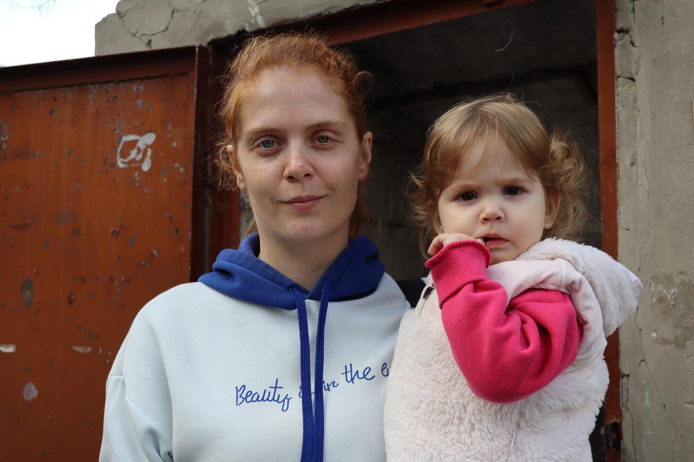 Anastasiia tillsammans med sin dotter utanför familjens hem i Derhachi i Charkivregionen. Huset skadades av beskjutning, och det är svårt att hålla det varmt under vintern. Foto: Inha Musiiuk/NRC