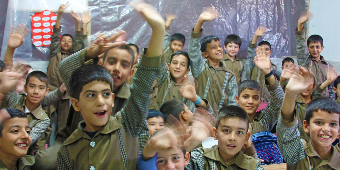Students waving in a renovated classroom at Ahmadlou School in Afghanistan.