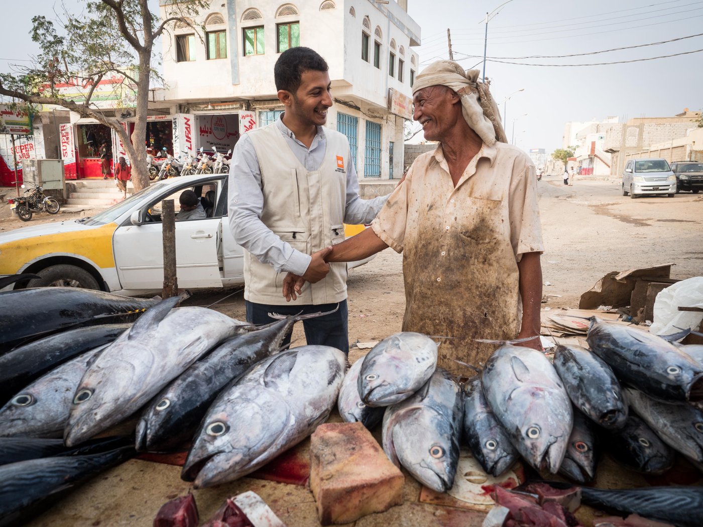 Abdohamid (57 years old – not an IDP). 
He worked with fishing authority (governmental sector) and retired.
He has seven children and all the retired salaries of the government sector are little without incentives; therefore, he looked for another source of income covering a shortage.

He has now started working with a mobile trader as an assistant, where they buy the fish whole sale from the fish market and then sell to customers.

This fish markets Al Hotta Lahj (South Yemen) was established back in 1979 by the Yemeni Government, to provide a market place to boost the fishing sector. Unfortunately, for many years the market remained closed or dysfunctional due to successive conflicts and wars in the area. During the 2015 conflict the building was damaged resulting in its complete closure.

Abdohamid and NRC Food security and Livelihood officer  Amr Al-Saqqaf is greeting.

Photo: Ingrid Prestetun/NRC