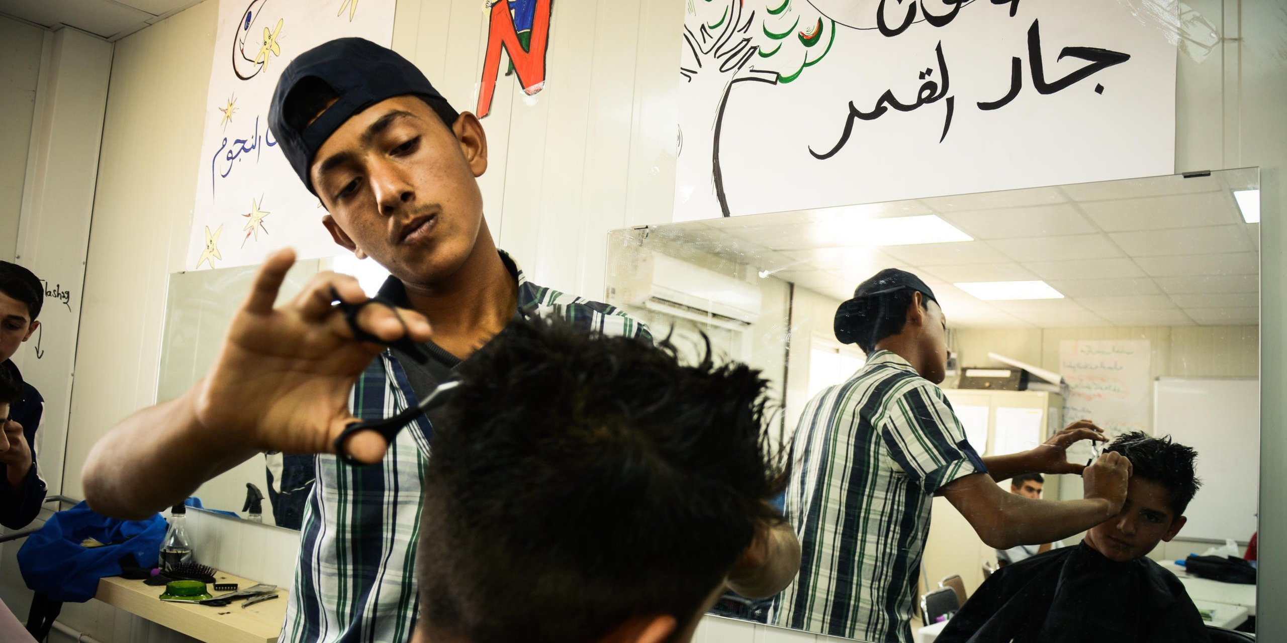 Ameer*, a 14-year-old boy having his hair cut by a Syrian refugee youth at NRC's youth training centre in Azraq refugee camp in Jordan. 

Ameer told us that he wants to be enrolled in this course because he used to work in his father's barber shop back in Syria, and would like to learn more here. Since he attends school in the camp, and does not fit the target age group for the centre, he cannot enroll. "Well, hopefully I can practice this skill when I'm back in Syria instead of here", says Ameer.

The youth training centre allocates one day each month for camp residents to come and have a free haircut at the site. 

*NRC changed all the names to protect the identity of those featured in this piece

July 1, 2015
Hussein Amri / NRC Jordan